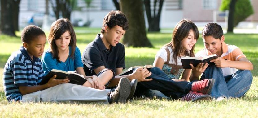 Diverse young students reading outdoors