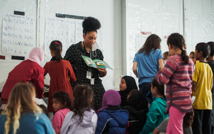 Task Force Pickett personnel reads stories to elementary school-age Afghan evacuee children in a classroom at Fort Pickett, with educational English alphabet posters in the background.