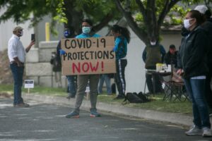 Immigrant workers holding a "COVID-19 Protections NOW!"