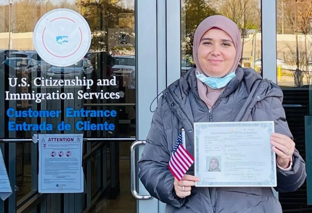 Amani holding a certificate of citizenship outside a USCIS building
