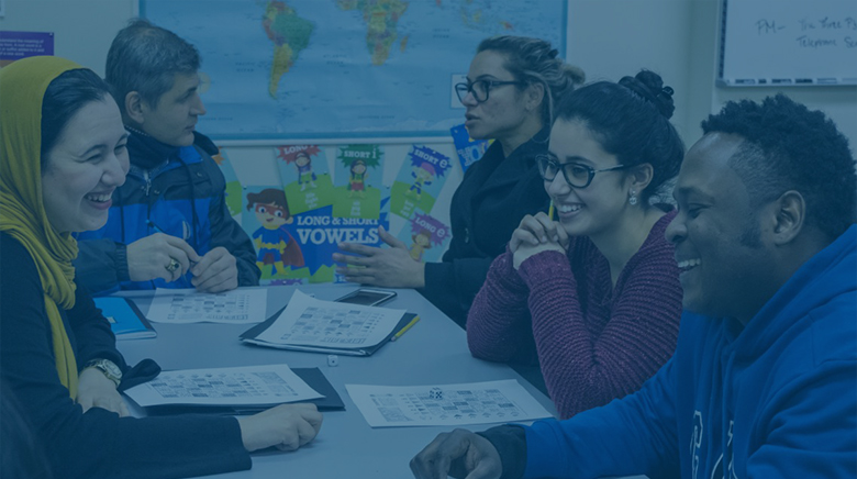 A group of immigrant students in a classroom smiling, talking and laughing with one another.