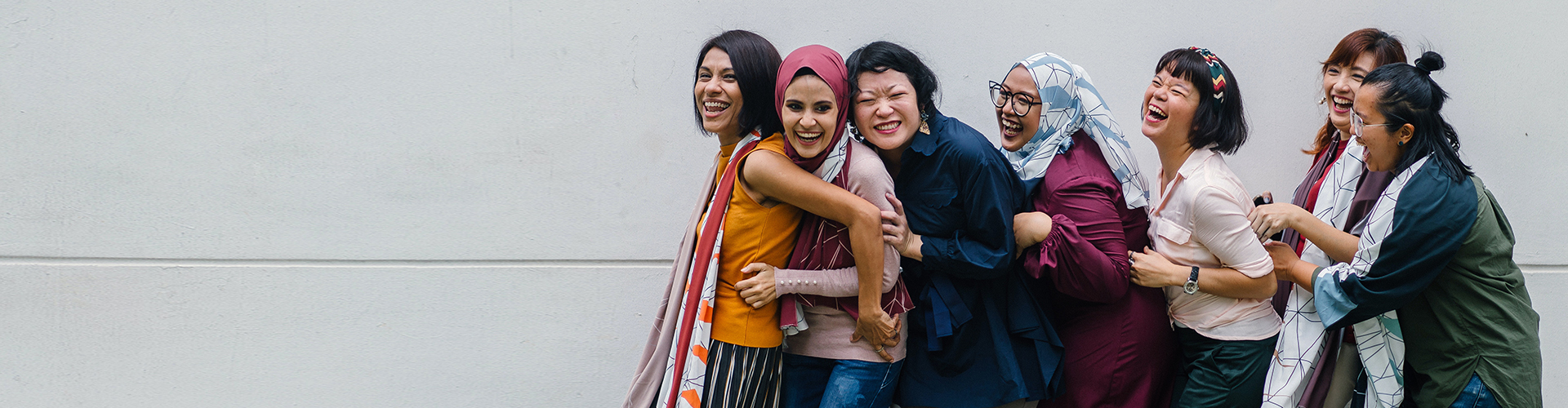 A group of diverse young adults smiling and laughing while hugging each other in a line.