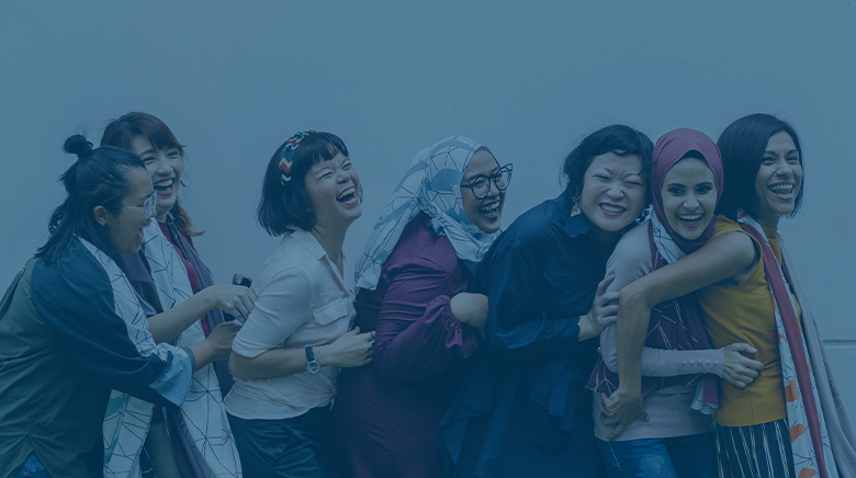 A group of diverse young adults smiling and laughing while hugging each other in a line.