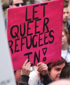 A protest featuring the sign saying, "LET QUEER REFUGEES IN!"