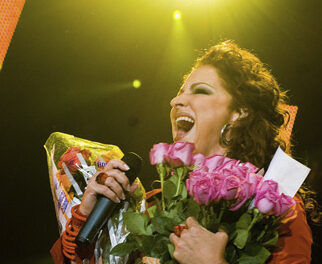 Gloria Estefan holding a microphone and flowers