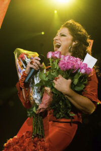 Gloria Estefan holding a microphone and flowers