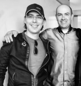 Jordi Munoz and Chris Anderson posing for a picture. Jordi on the left is wearing a baseball cap and jacket. Chris on the right has his arm around Jordi.