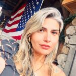 A selfie of a woman in front of a big American flag.