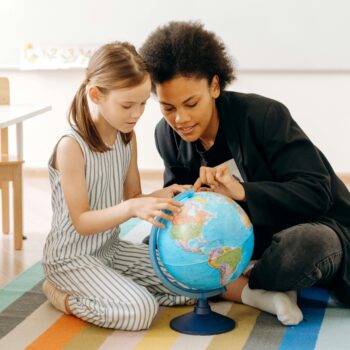 A teacher pointing out a spot on a globe to a young student.