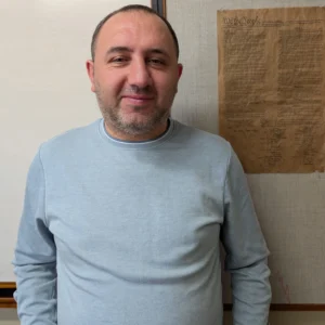 A man in a light blue shirt stands in front of a wall with a small copy of the U.S. Constitution.