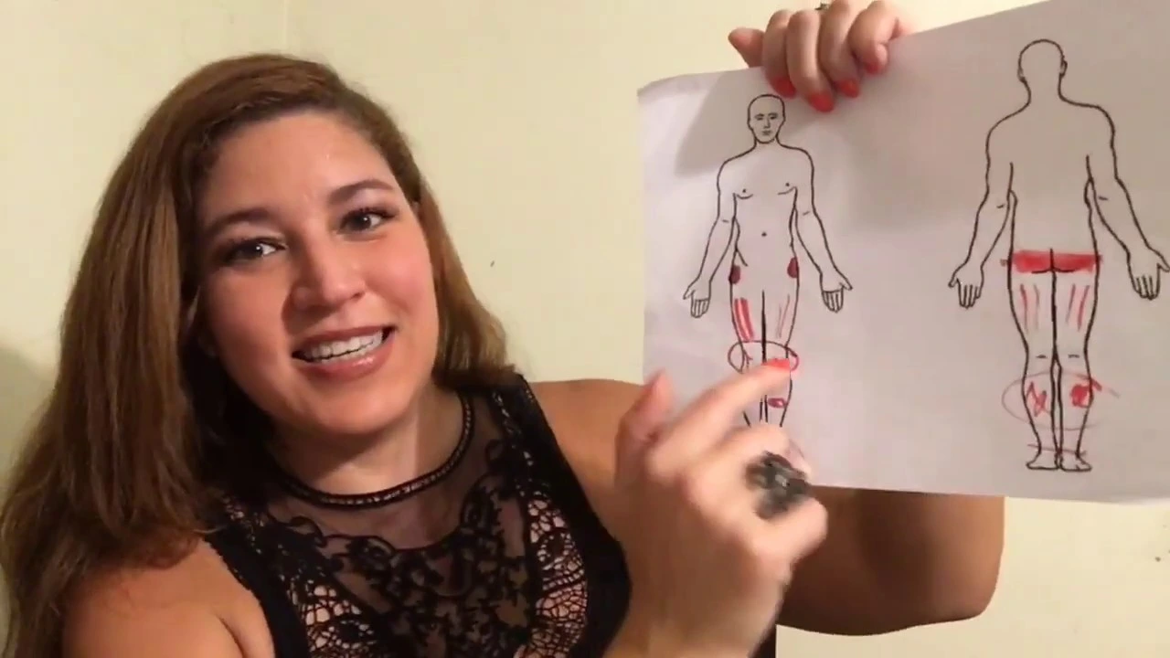 A woman holds up a piece of paper with drawings of the human body on it in an ESOL lesson. She's pointing to the leg and looking at the camera.