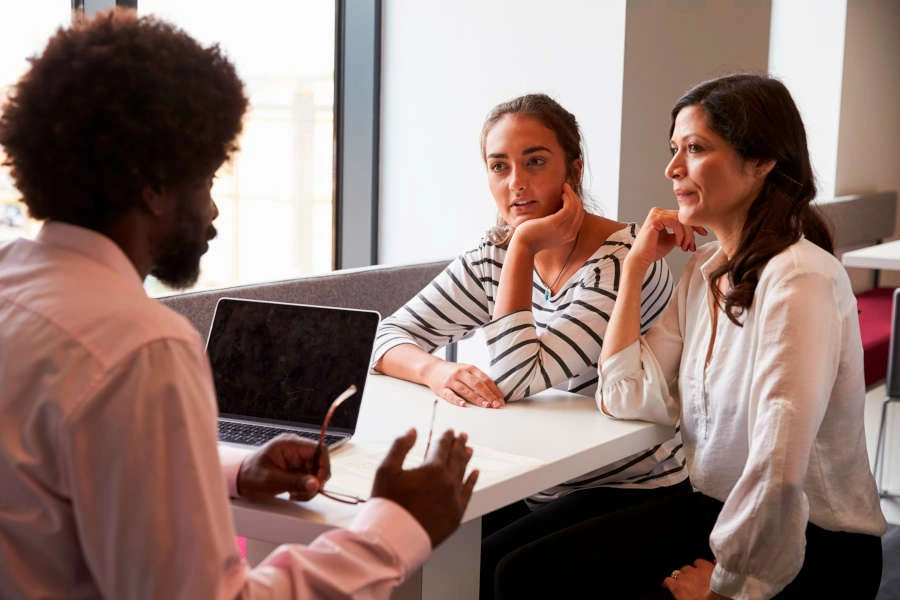 A man talking to a woman and a teen over a table.