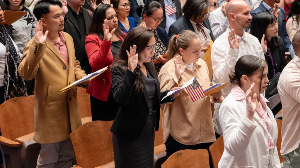 A huge group of immigrants in an auditorium taking the citizenship oath.
