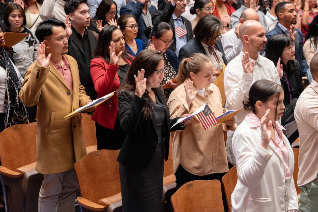 A huge group of immigrants in an auditorium taking the citizenship oath.