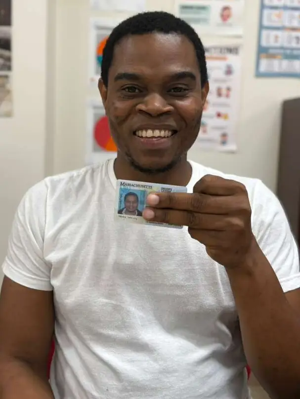 A Haitian man holding a Massachusetts driver's license and smiling.